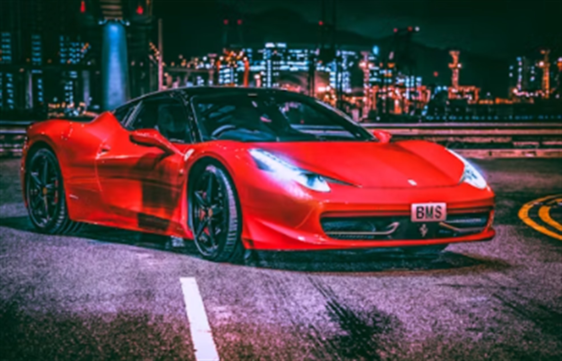 Red Ferrari parked at night with a glowing city skyline behind it